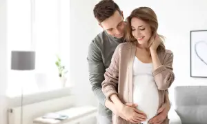Mężczyzna obejmuje brzuch swojej ciężarnej żony, okazując troskę i miłość. To piękny obraz opieki nad żoną po porodzie, pełen nadziei na przyszłość.