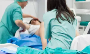 Personel medyczny zajmuje się pacjentką po porodzie. Widoczne są zielone fartuchy i sprzęt medyczny.