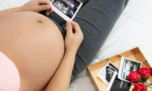 Kiedy widać brzuch ciążowy, przyszła mama trzyma zdjęcie USG. Obok leży pudełko z kolejnymi zdjęciami i czerwonymi różami.