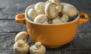 Pomarańczowa miseczka pełna świeżych pieczarek, jakby w ciąży z nowymi smakami. Kilka pieczarek leży obok na drewnianym blacie.