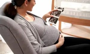 Ciężarna kobieta z uśmiechem ogląda zdjęcia z usg wątroby swojego dziecka.