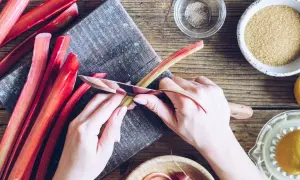 Rabarbar w ciąży, przygotowywany do ciasta. Dłonie obierają łodygi, obok cukier, cytryna i przyprawy.