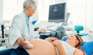 Lekarka wykonuje USG brzucha uśmiechniętej pacjentki. To już 5 miesiąc ciąży, a na ekranie widać obraz dziecka.