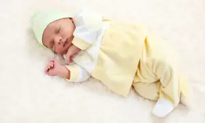 Śpiący wcześniak w żółtym ubranku i zielonej czapeczce, otulony miękkim kocykiem.