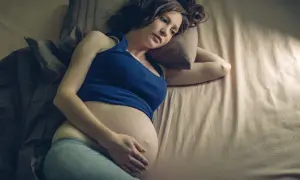 Zmęczona kobieta w zaawansowanej ciąży leży na łóżku, próbując zasnąć. Bezsenność w ciąży to częsty problem.