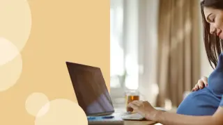 Kobieta w ciąży przy laptopie, która uśmiecha się, dotykając brzucha. Dowiaduje się, jak liczyć ruchy dziecka.