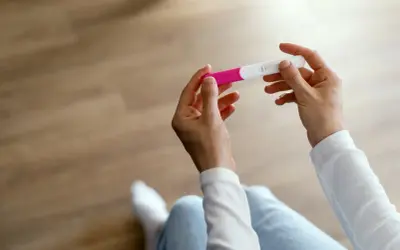 Dłonie trzymające test ciążowy. Wynik wskazuje na wczesny etap, być może 1 tydzień ciąży.
