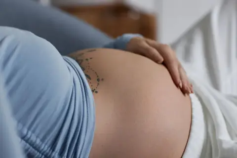 Dłoń delikatnie głaszcze ciążowy brzuch, na którym widnieje tatuaż. To piękny obraz stawiania się macicy i oczekiwania na nowe życie.
