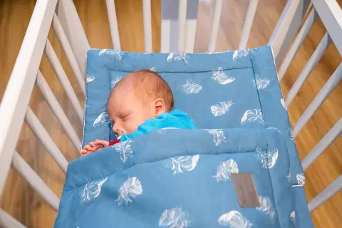 Śpiące dziecko w niebieskim otulaczu z piórkami, z pewnością czeka na swoje pierwsze pępkowe.