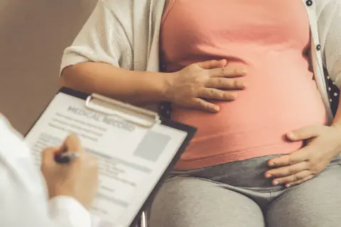 Lekarz notuje dane pacjentki, która trzyma dłoń na brzuchu. Obliczenia terminu porodu opierają się na regule Naegelego.