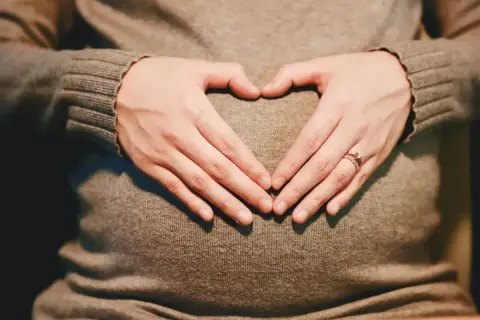 Dłonie tworzą serce na brzuchu ciężarnej. Od kiedy pojawiają się skurcze Braxtona Hicksa?