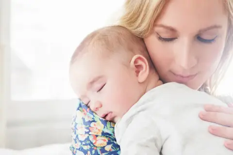 Samotna matka tuli śpiące dziecko. Delikatne światło otula ich spokój.