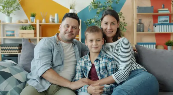 Szczęśliwa rodzina: tata, mama i syn siedzą na kanapie. Choć nie da się określić, ile kosztuje dziecko, miłość i radość są bezcenne.