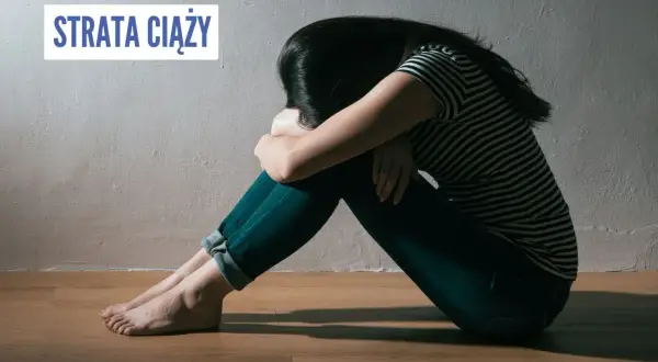 Smutna kobieta siedzi skulona na podłodze, przeżywając stratę ciąży.