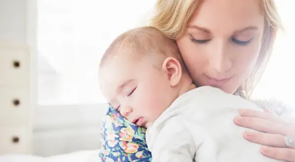 Samotna matka tuli śpiące dziecko. Delikatne światło otula ich spokój.