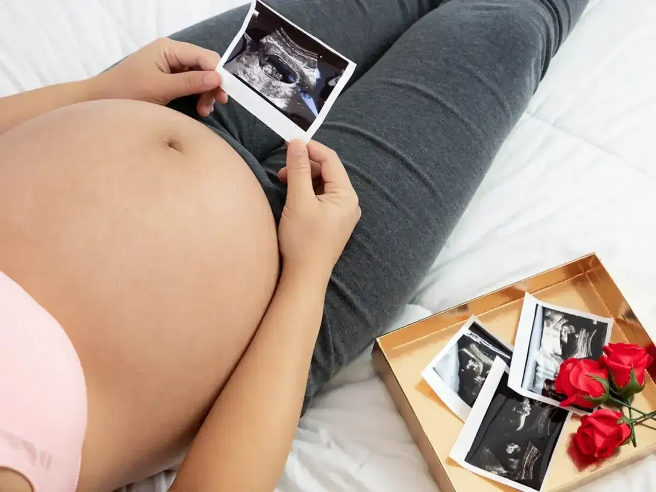 Kiedy widać brzuch ciążowy, przyszła mama trzyma zdjęcie USG. Obok leży pudełko z kolejnymi zdjęciami i czerwonymi różami.