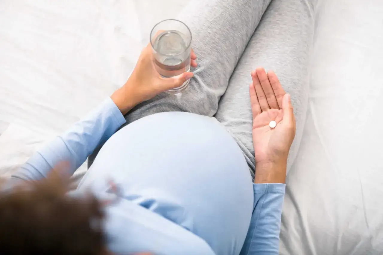 Kobieta w ciąży trzyma tabletkę i szklankę wody. Ostrożne przyjmowanie antybiotyku w ciąży jest kluczowe dla zdrowia matki i dziecka.