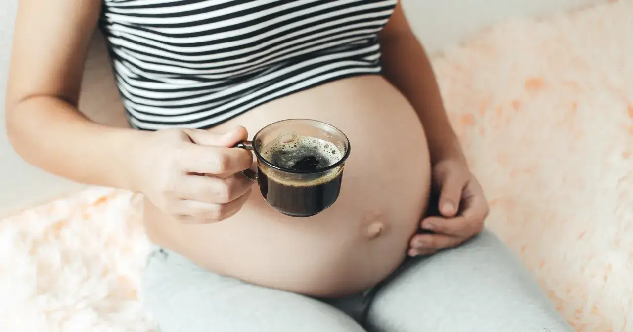 Ciężarna kobieta trzyma filiżankę kawy, zastanawiając się, czy można pić kawę w ciąży.