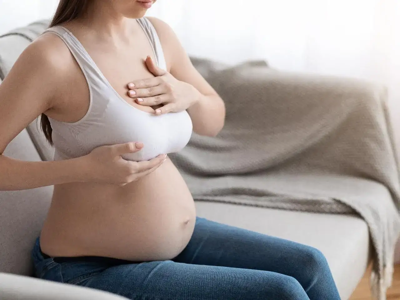 Kobieta w ciąży delikatnie dotyka swoich piersi. Zmiany w sutkach w ciąży są naturalne.