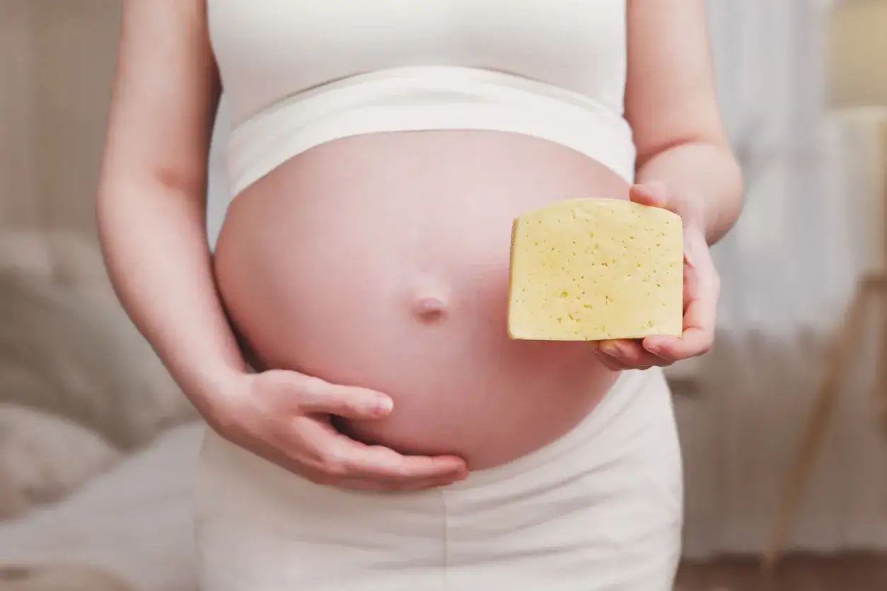 Ciężarna kobieta trzyma kawałek żółtego sera obok swojego brzucha.