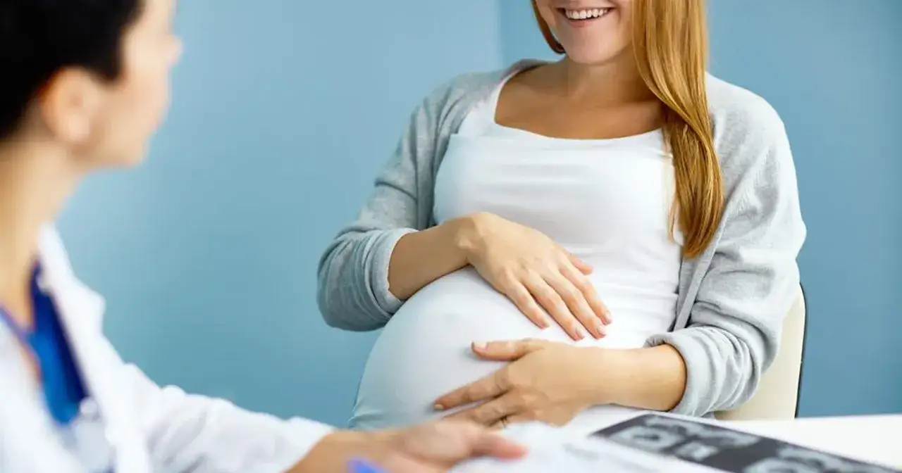 Ciężarna kobieta rozmawia z lekarzem, który bada jej brzuch. To może być moment, gdy omawiają, jak wygląda odejście wód płodowych.