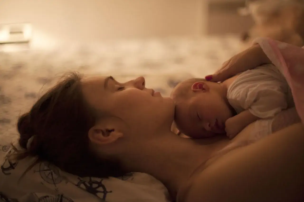 Ciepły, intymny moment w okresie po porodzie. Mama tuli śpiące maleństwo do piersi, czując jego oddech.