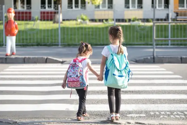 Dwie dziewczynki z plecakami idą przez pasy. Od ilu lat dziecko może samo chodzić po mieście? Zależy od dziecka i jego dojrzałości.